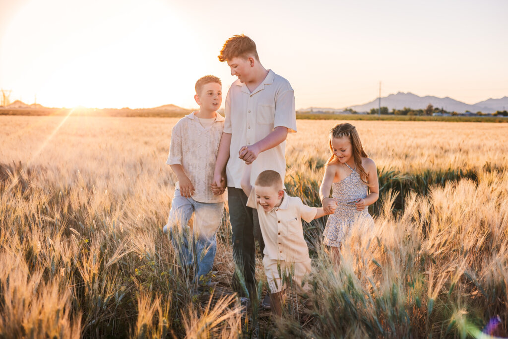 Kids walking through wheat fields and holding hands at golden hour in Buckeye, Arizona.