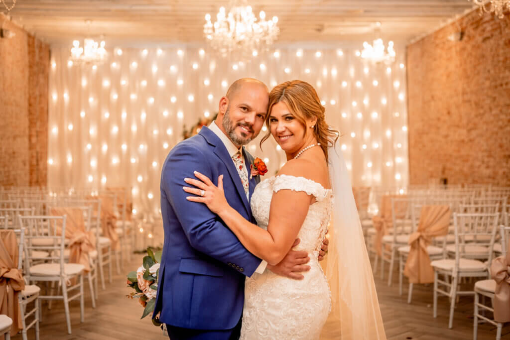 Close up photo of wedding couple with red brick and twinkling lights and chandelier