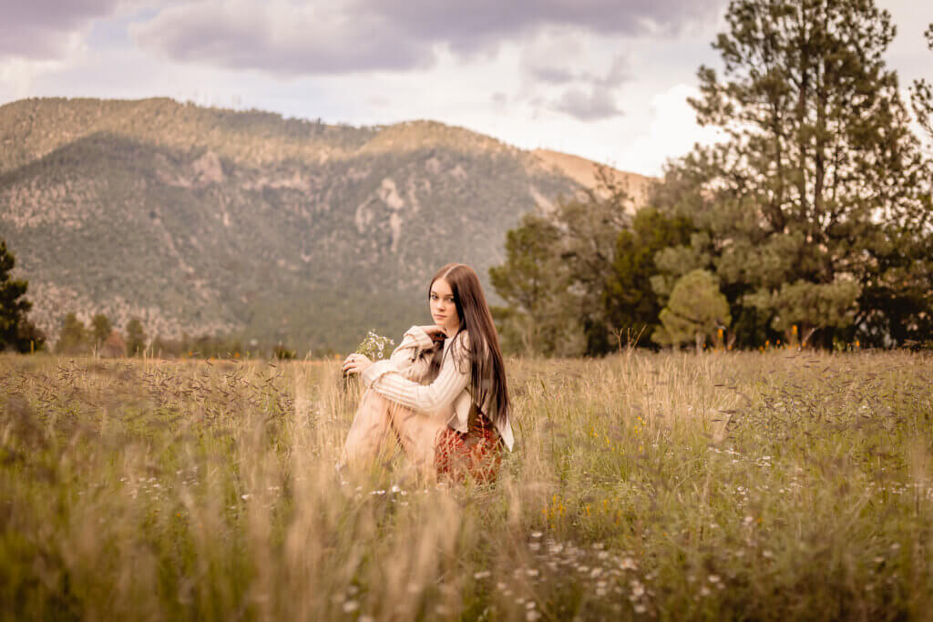photo of teen holding daisies with a wide mountain background and grassy fields at Buffalo Park in Flagstaff, Arizona