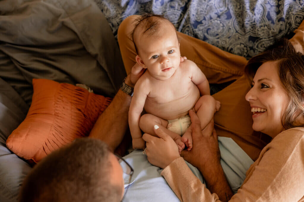 lifestyle newborn photo of parents looking at baby and baby looking at photographer
