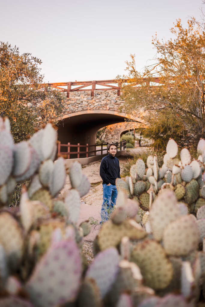 Photo of senior portrait with guy behind prickly pear cacti and in front of bridge in Scottsdale, AZ