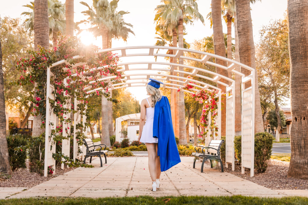 photo of senior grad holding gown over her shoulder in green flower area with palm trees