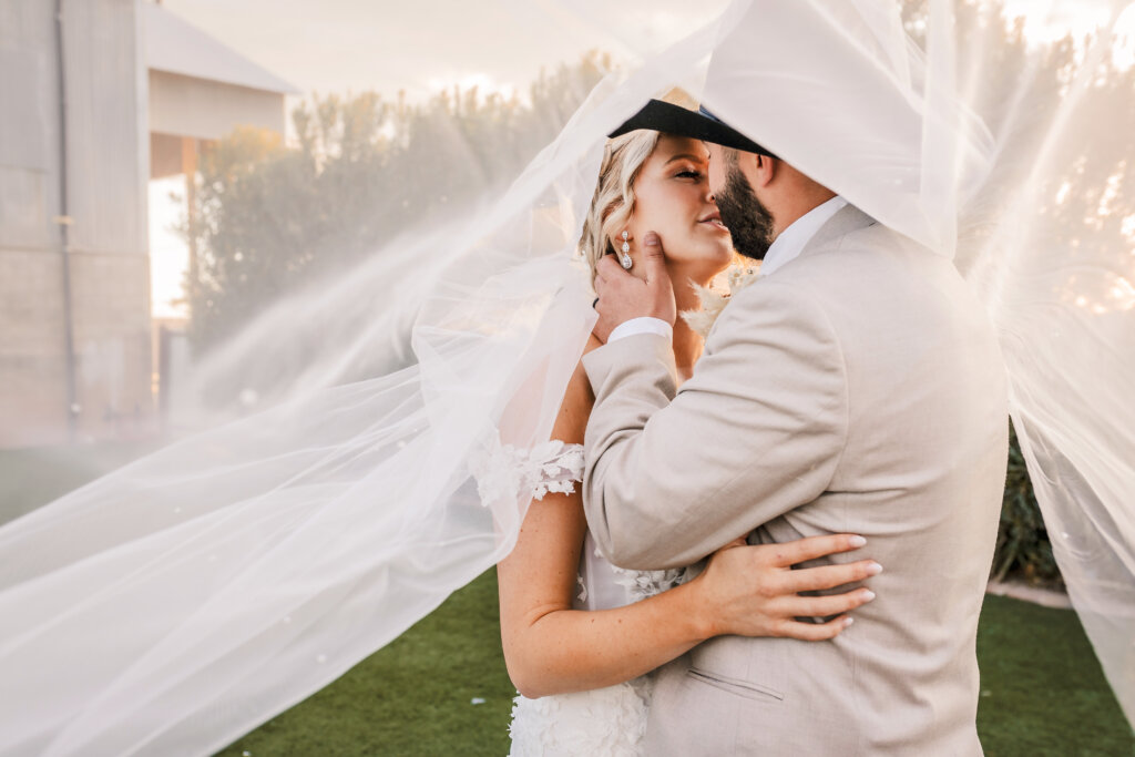 Photo of wedding couple kissing under veil at Golden Hour at the Big Tin Cotton Gin in San Tan Valley, AZ