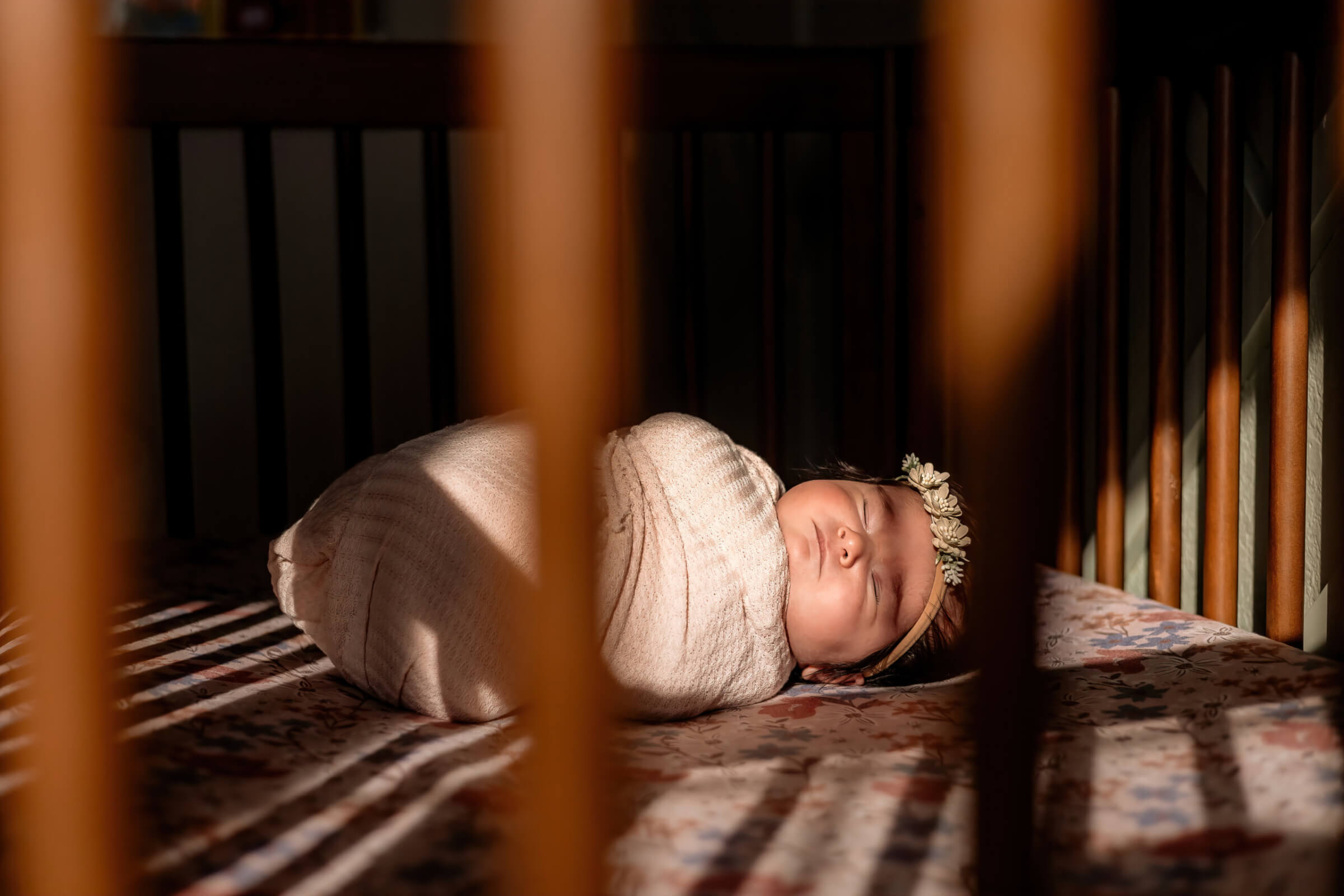 Photo of newborn baby girl in her crib with sun shining through.