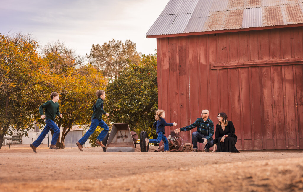 Family photography with Phoenix family at Manistee Ranch Park in Glendale, AZ with red barn in background.