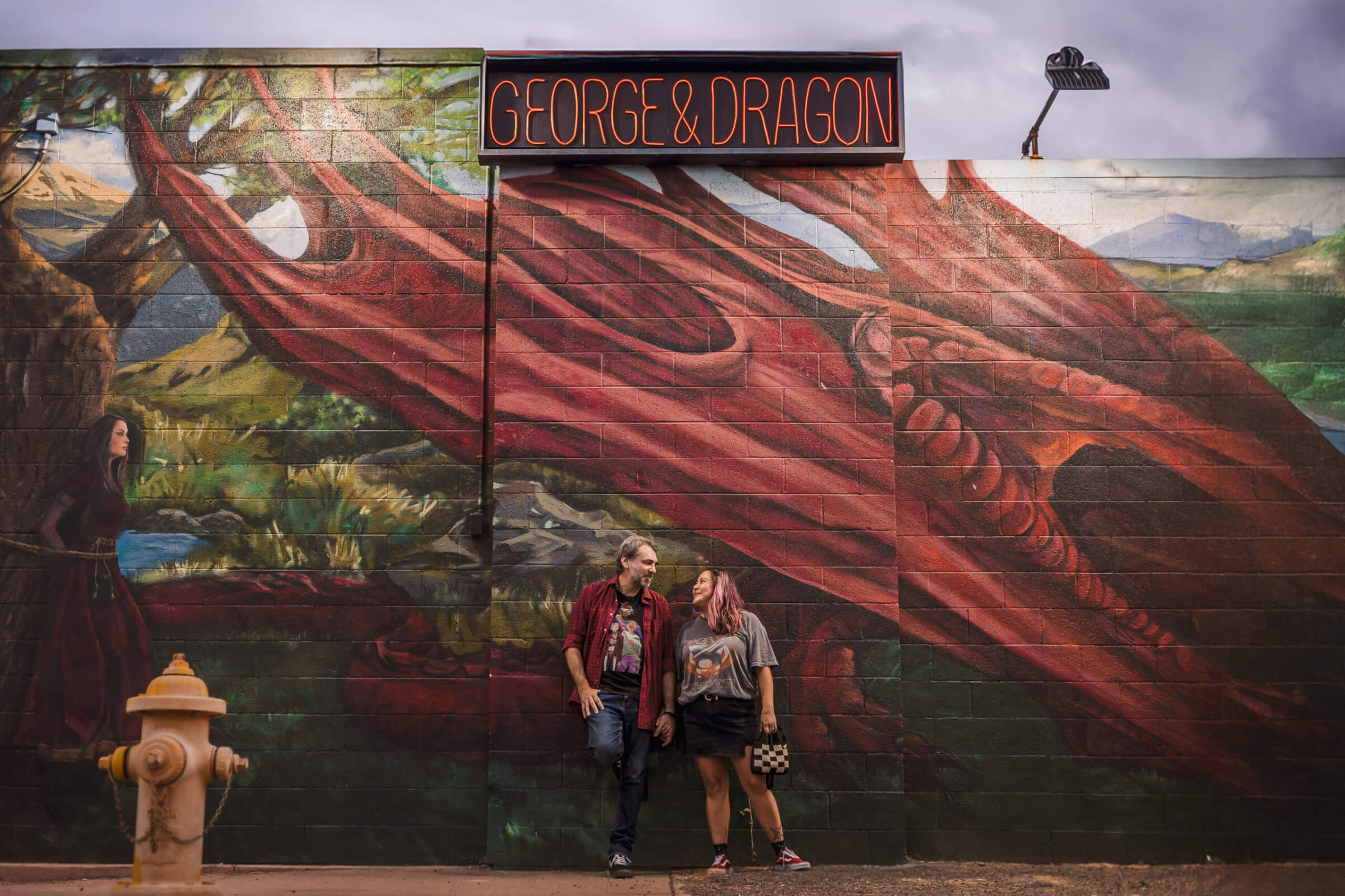 Phoenix engaged couple up against wall mural of the George and Dragon English Pub in Downtown.