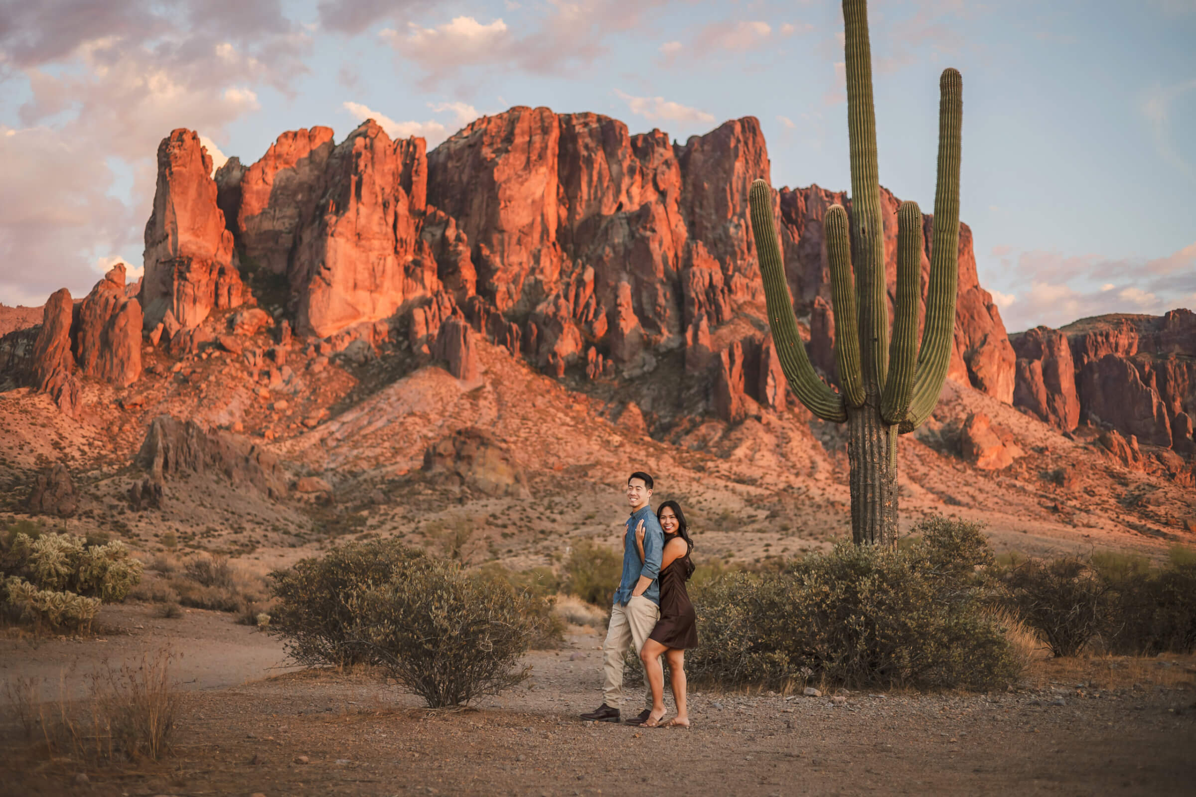 Beautiful wide gorgeous landscape photo of a newly engaged Phoenix couple standing in front of the Superstition Mountains in Lost Dutchman State Park in Apache Junction, Arizona - photographed by Phoenix Photographer.