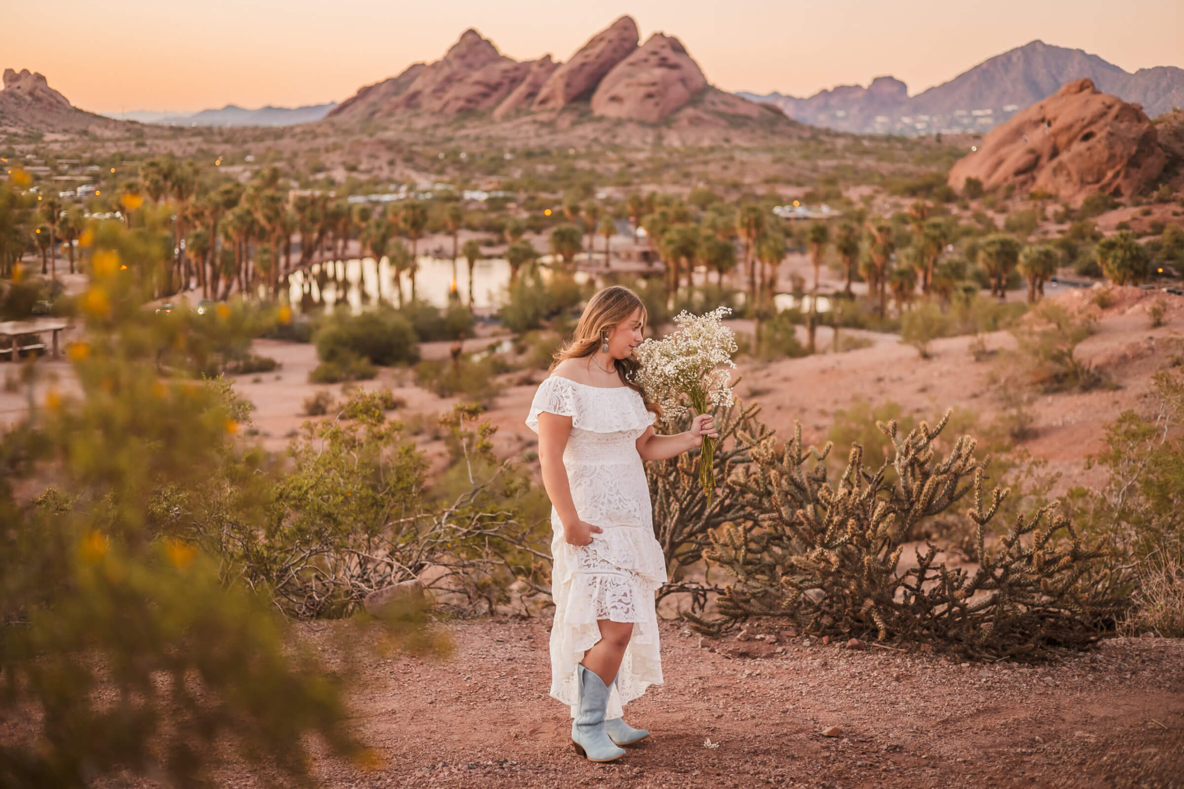 Senior portrait of girl smelling baby's breath flowers with the Papago Mountains in the background at sunset.
