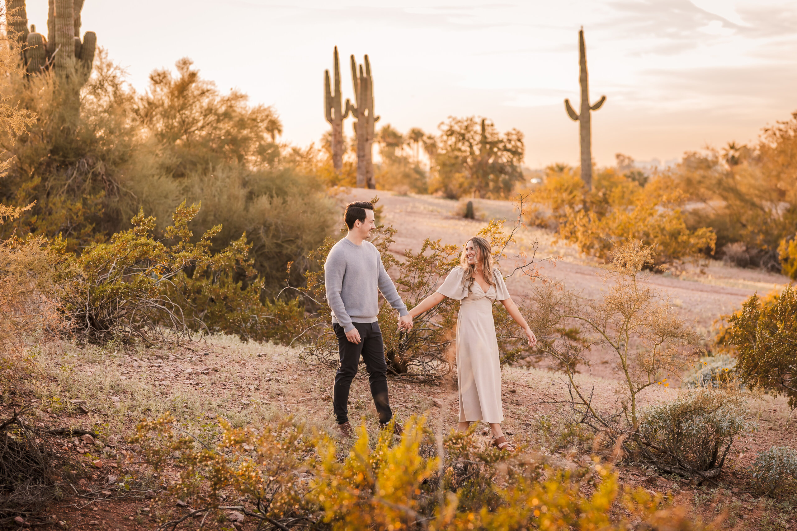 Engagement photo of couple walking together through Papago Park with warm sun and desert scenery