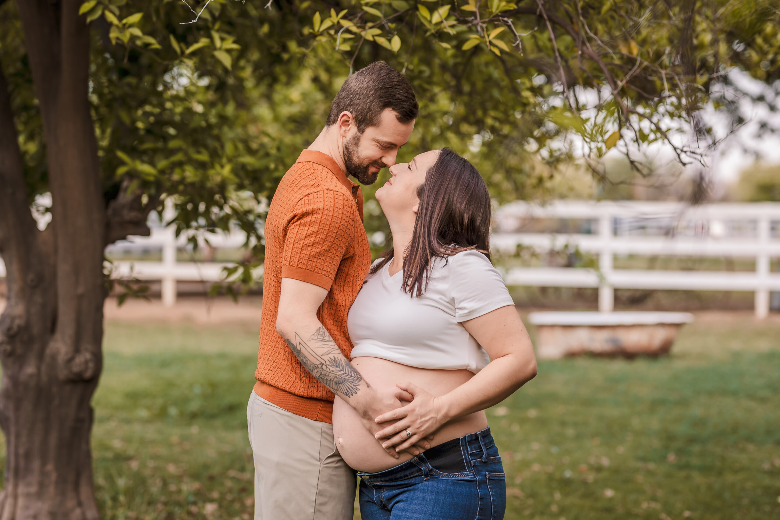 Intimate photos of expecting couple with hands on belly with green background and white fence at Manistee Ranch.