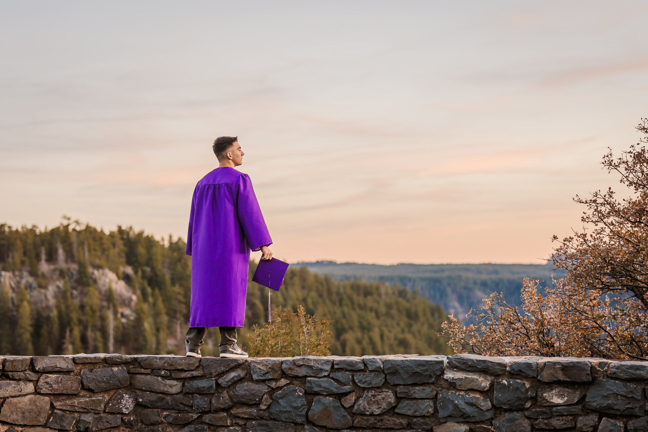 Senior portrait taken at Oak Creek Vista near Sedona with high school senior standing on rock wall overlooking canyon.