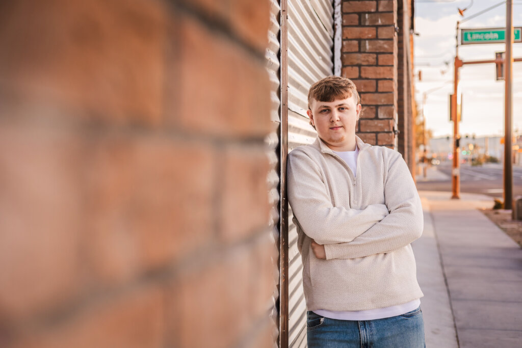 Urban photo of senior high school graduate leaning on brick building in Downtown Phoenix, for an edgy modern look.