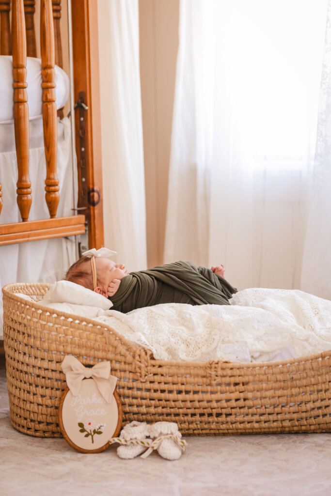 Newborn baby swaddled in olive green wrap and laying in a moses basket in the soft natural light at Studio House AZ, photographed by Memories by Candace.