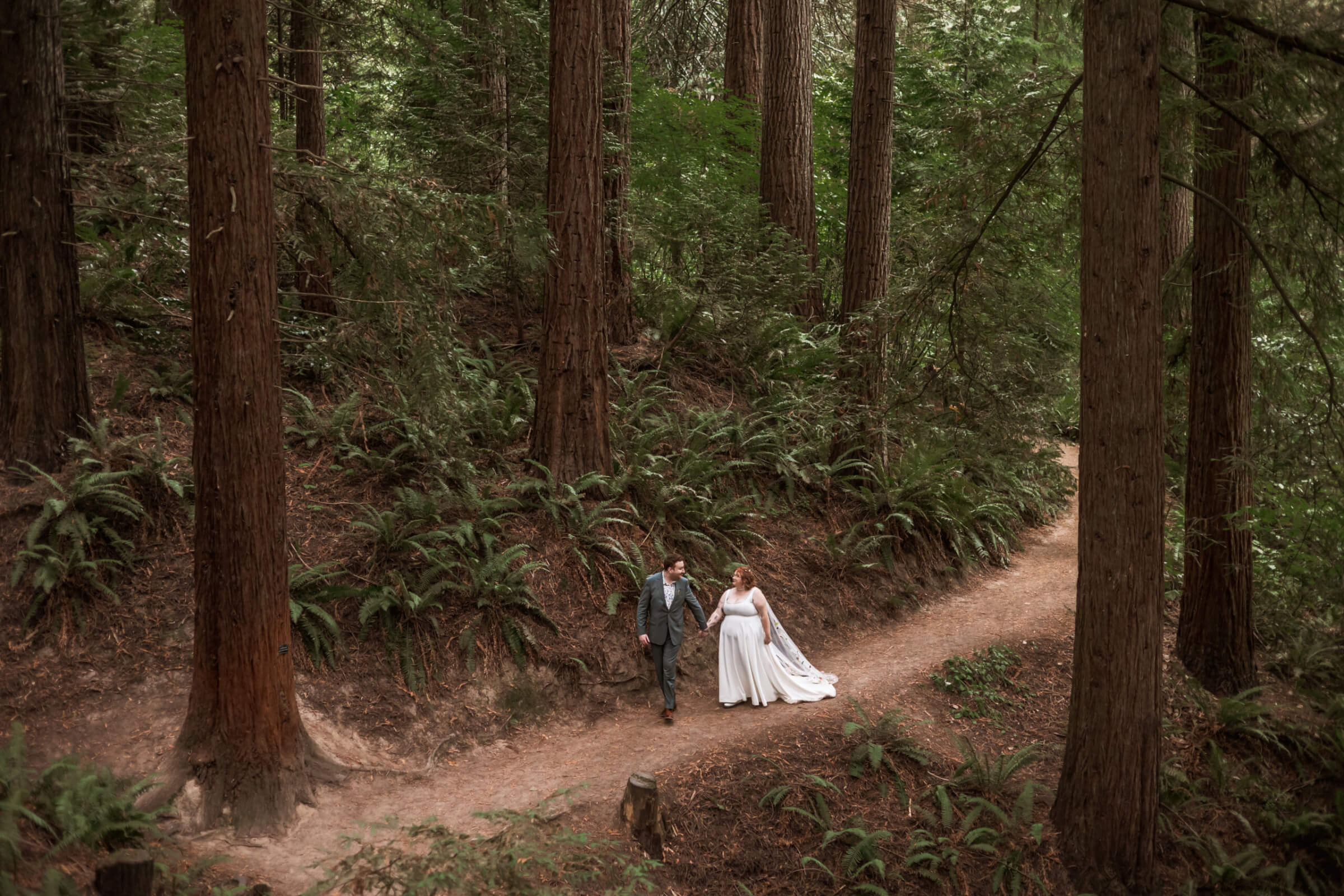 Wide cinematic photo of bride and groom walking through the forest in Portland, Oregon.