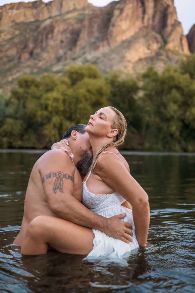 Intimate and romantic photo of Phoenix couple that have been together for 19 years. Man's holding his wife in the water as the river surrounds them and kissing her neck as she holds onto his neck.
